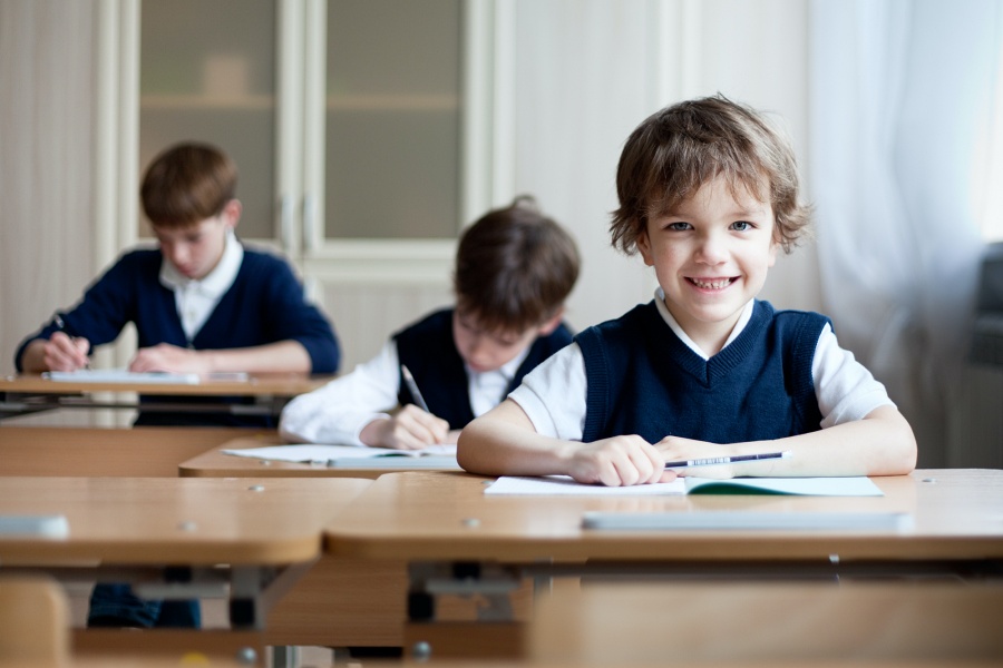 małe, elegancko ubrane dzieci siedzą w ławkach szkolnych i piszą egzamin